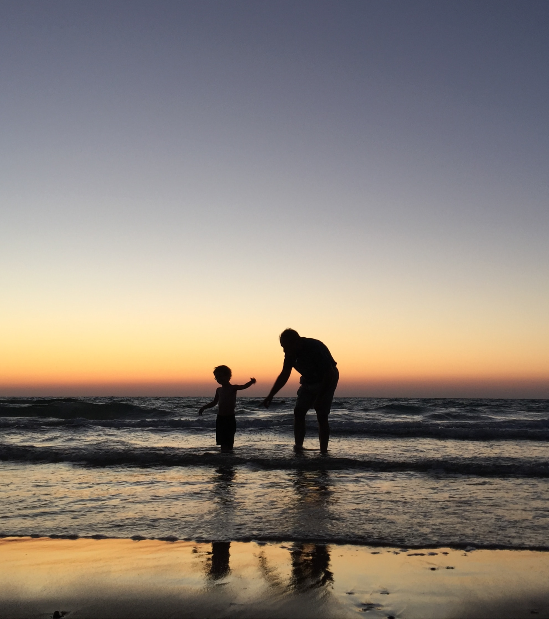 A parent and child together at the ocean at sunset